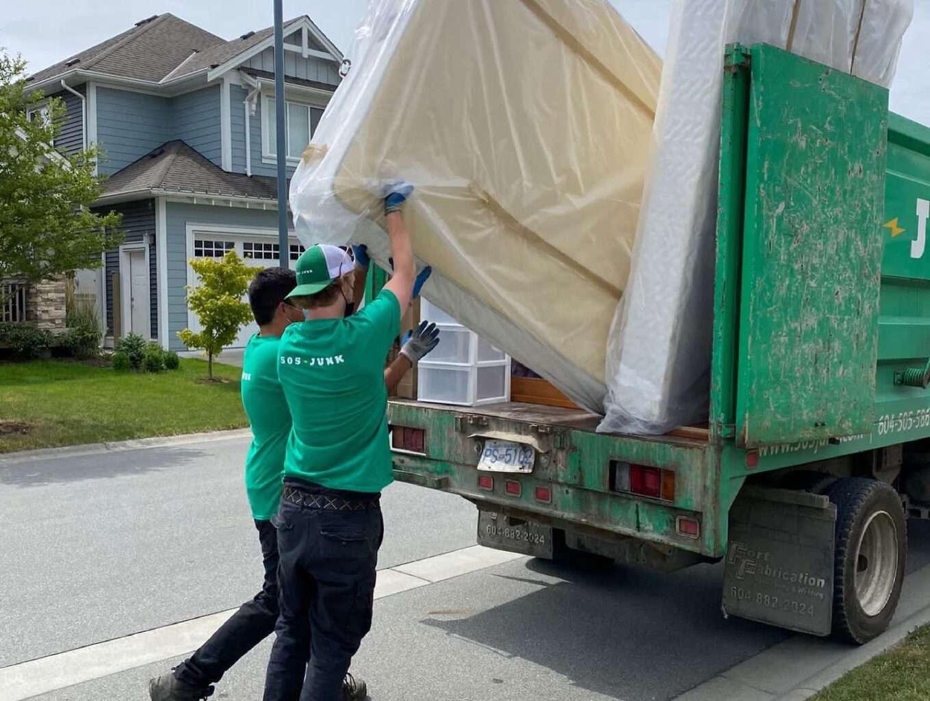 2 teammates lifting a mattress into a 505-Junk truck to be recycled.