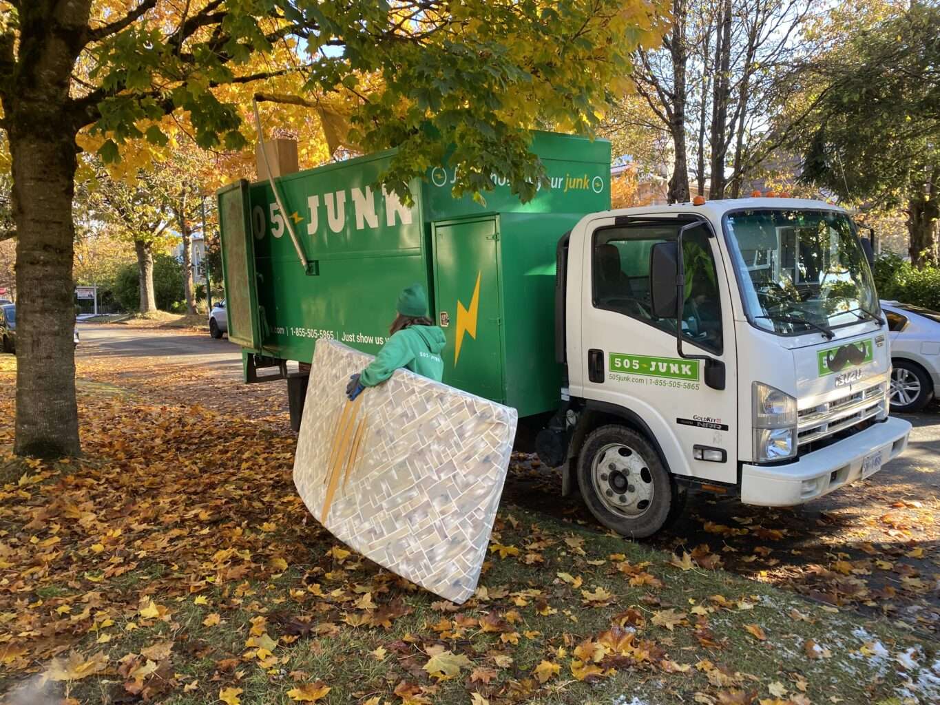 A 505-Junk truck in the fall leaves with an employee carrying a mattress to the truck.