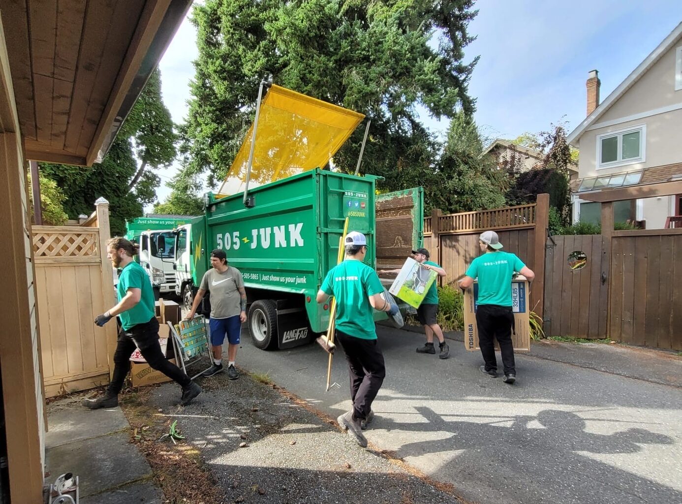 Four 505-Junk employees walking from the house to the truck with brooms and boxes in their hands while completing a downsizing clearout. 